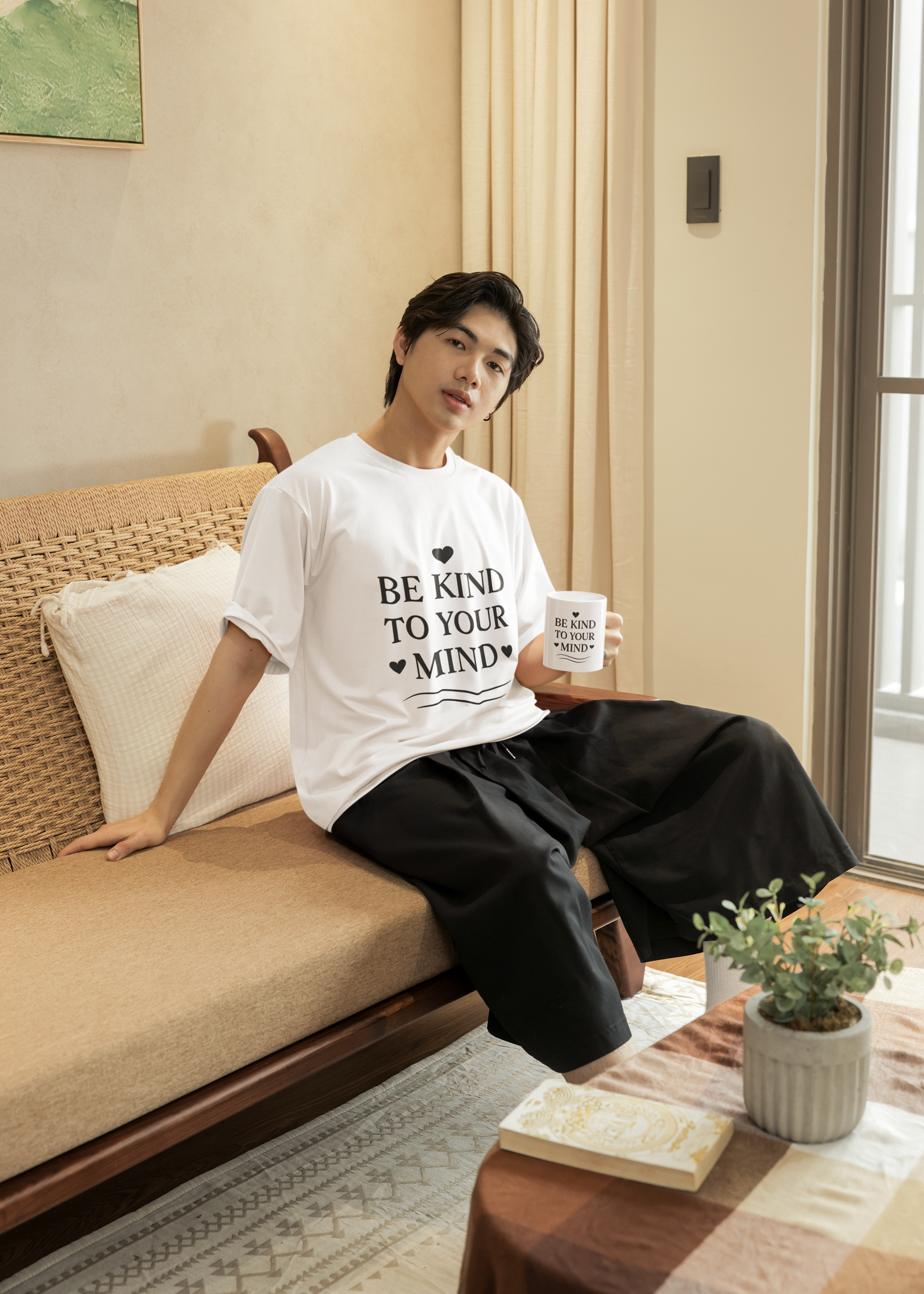 Be Kind to Your Mind - Man sitting on a couch wearing a white t-shirt with a motivational message, holding a mug.